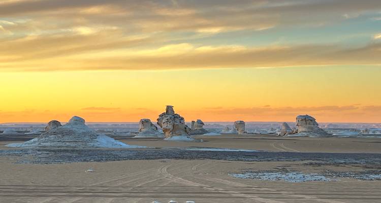 Golden sunset colors illuminate chalk spires across vast desert plain with soft clouds above.
