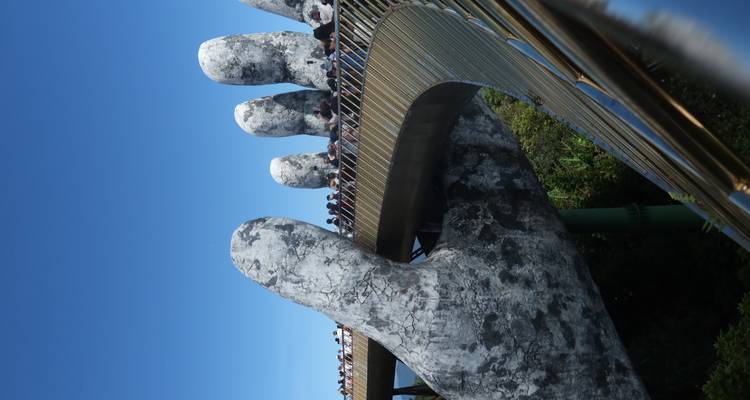 Crowds walk across Da Nang’s iconic Golden Bridge, held aloft by giant stone hands under a clear blue sky.