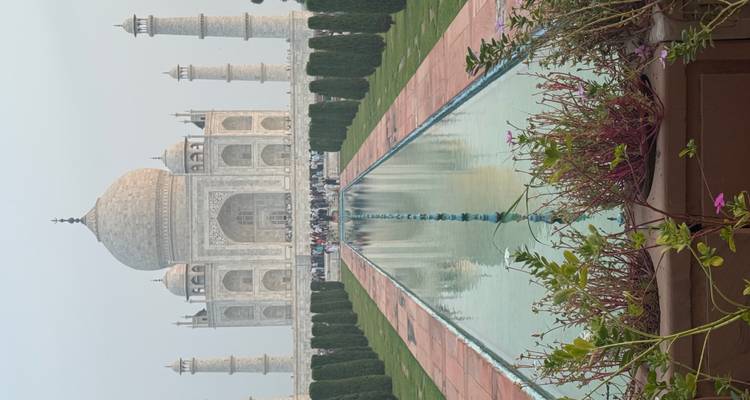 Le Taj Mahal se reflétant dans son bassin central avec des rangées de cyprès et des visiteurs au loin.