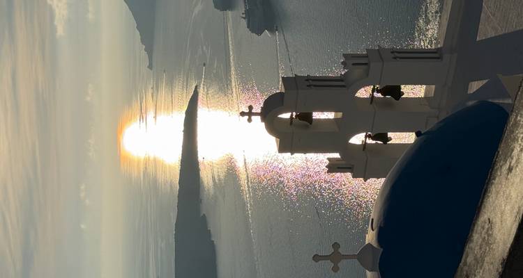 La tour blanche emblématique et le dôme bleu de Santorin surplombant la scintillante mer Égée au coucher du soleil.
