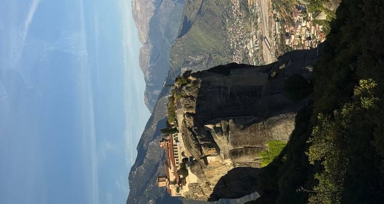 Monastère perché au sommet d'un énorme pilier rocheux dans la région des Météores avec des montagnes en arrière-plan.
