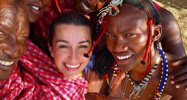 Un selfie joyeux avec un voyageur souriant entouré de compagnons Maasai vêtus de couleurs vives en shuka rouges éclatants et en bijoux perlés.