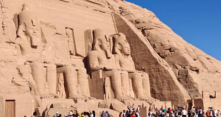 Grandiosa fachada del templo de Abu Simbel con cuatro estatuas colosales sentadas bañadas por la brillante luz del sol y multitudes abajo.