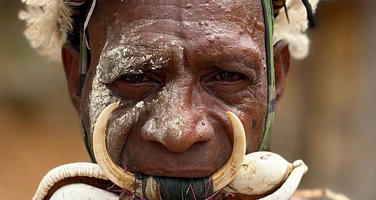 Retrato de un miembro de la tribu Asaro con la cara cubierta de arcilla y un adorno nasal ornamentado con colmillo.