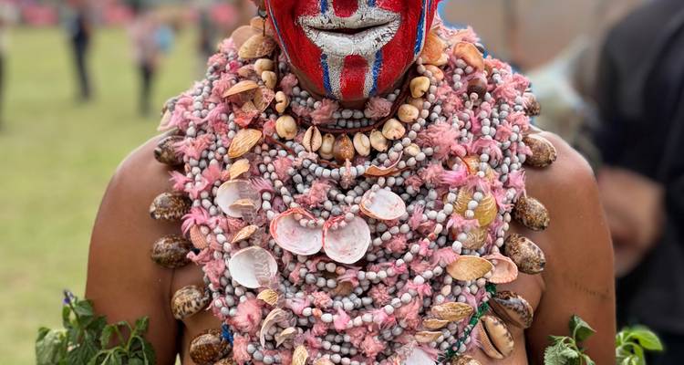 Artista de festival con pintura facial roja y azul brillante y un elaborado collar de conchas.