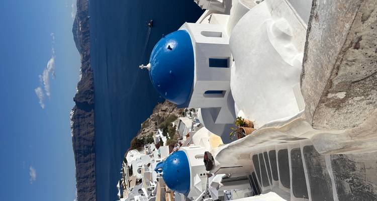 Los icónicos tejados de iglesias con cúpulas azules y las casas encaladas se descienden en cascada hacia el profundo mar Egeo azul en Oia.