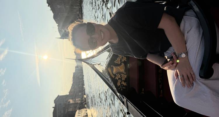 Eine Frau genießt eine Gondelfahrt auf einem venezianischen Kanal bei Sonnenuntergang mit goldenem Licht, das sich im Wasser spiegelt.