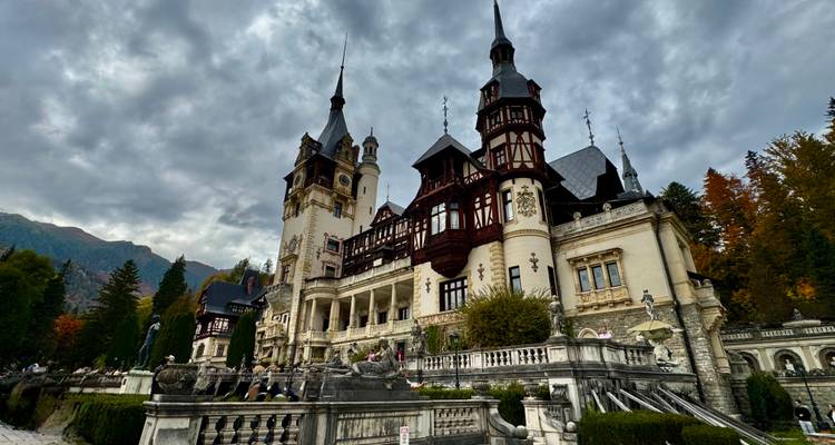 Grandioso Castillo Neorrenacentista Peles con torres ornamentadas contra un cielo dramático y montañas.