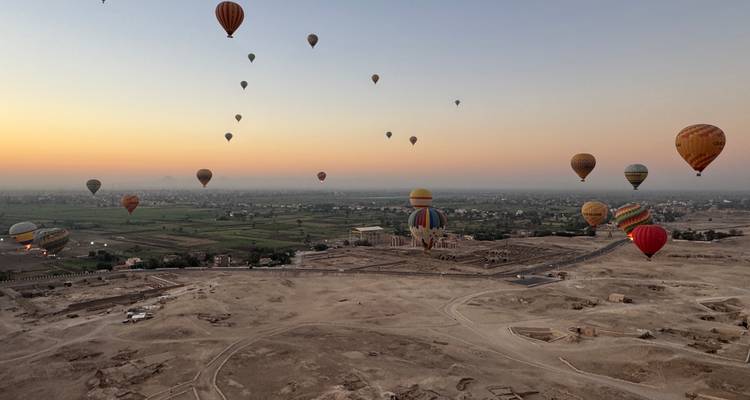 Des dizaines de montgolfières colorées s'élèvent au-dessus des ruines de Louxor à l'aube avec un ciel orange au-dessus des terres agricoles.