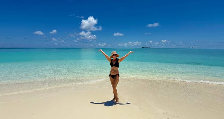 Une femme en bikini noir pose avec joie sur une plage de sable blanc immaculé aux eaux turquoise cristallines.