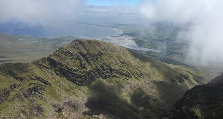 Berglandschap met bewolkte lucht en zee in de verte.