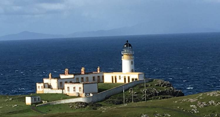 Ein abgelegener Leuchtturm auf einer grünen Klippe mit Blick aufs Meer.