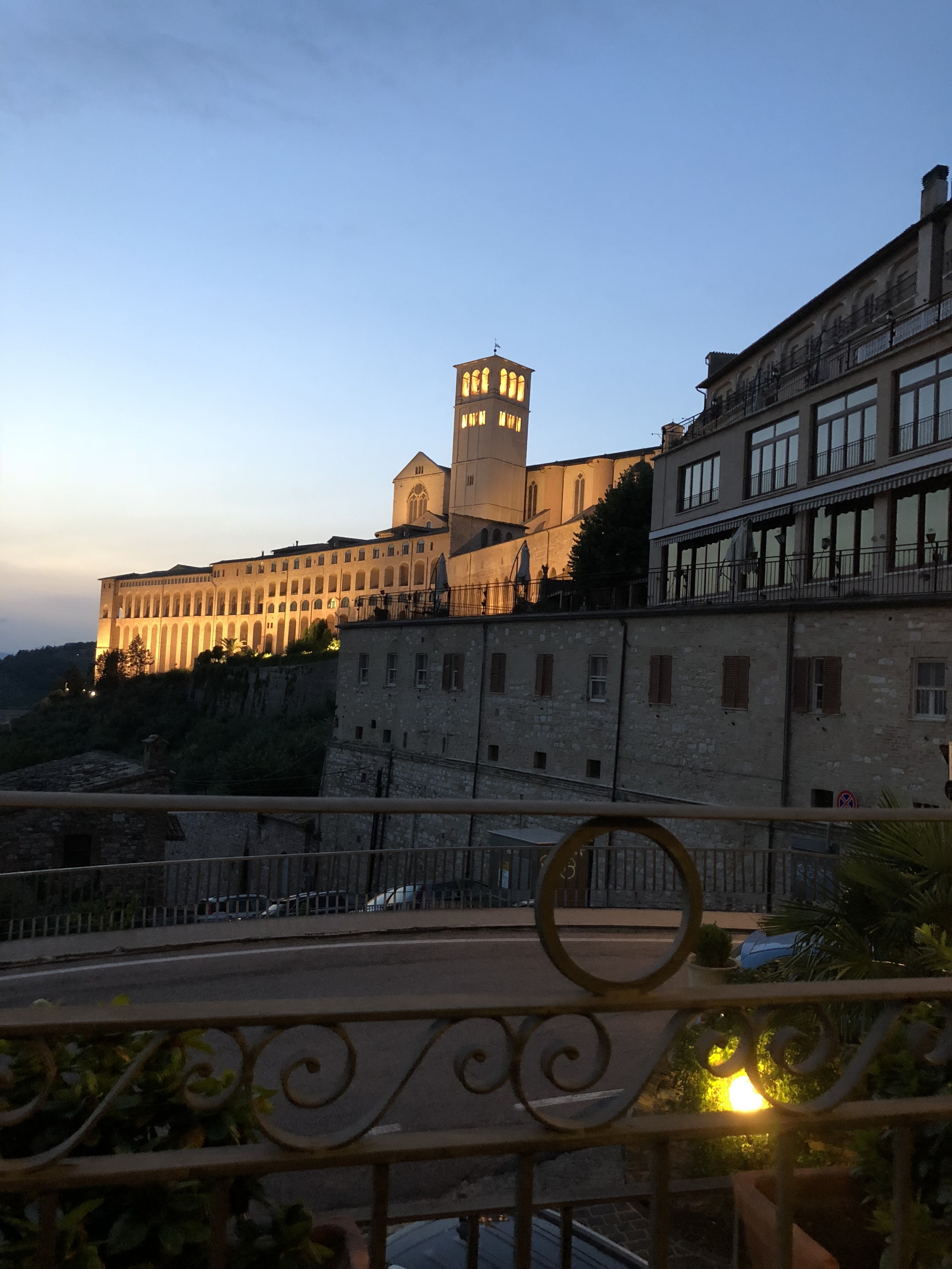 Large building with lights on at dusk overlooking a town.