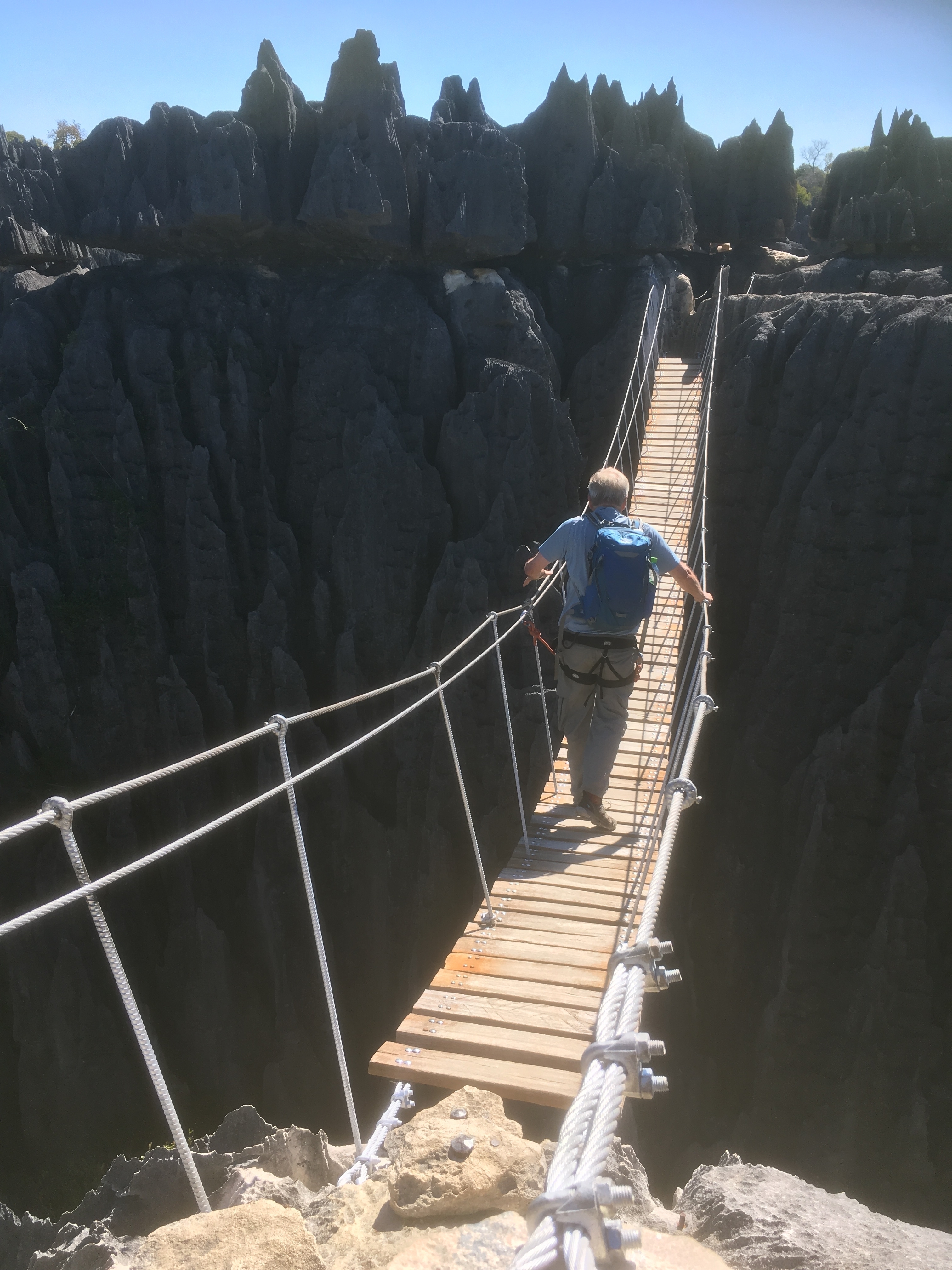 Person crossing a rope bridge over rock formations.