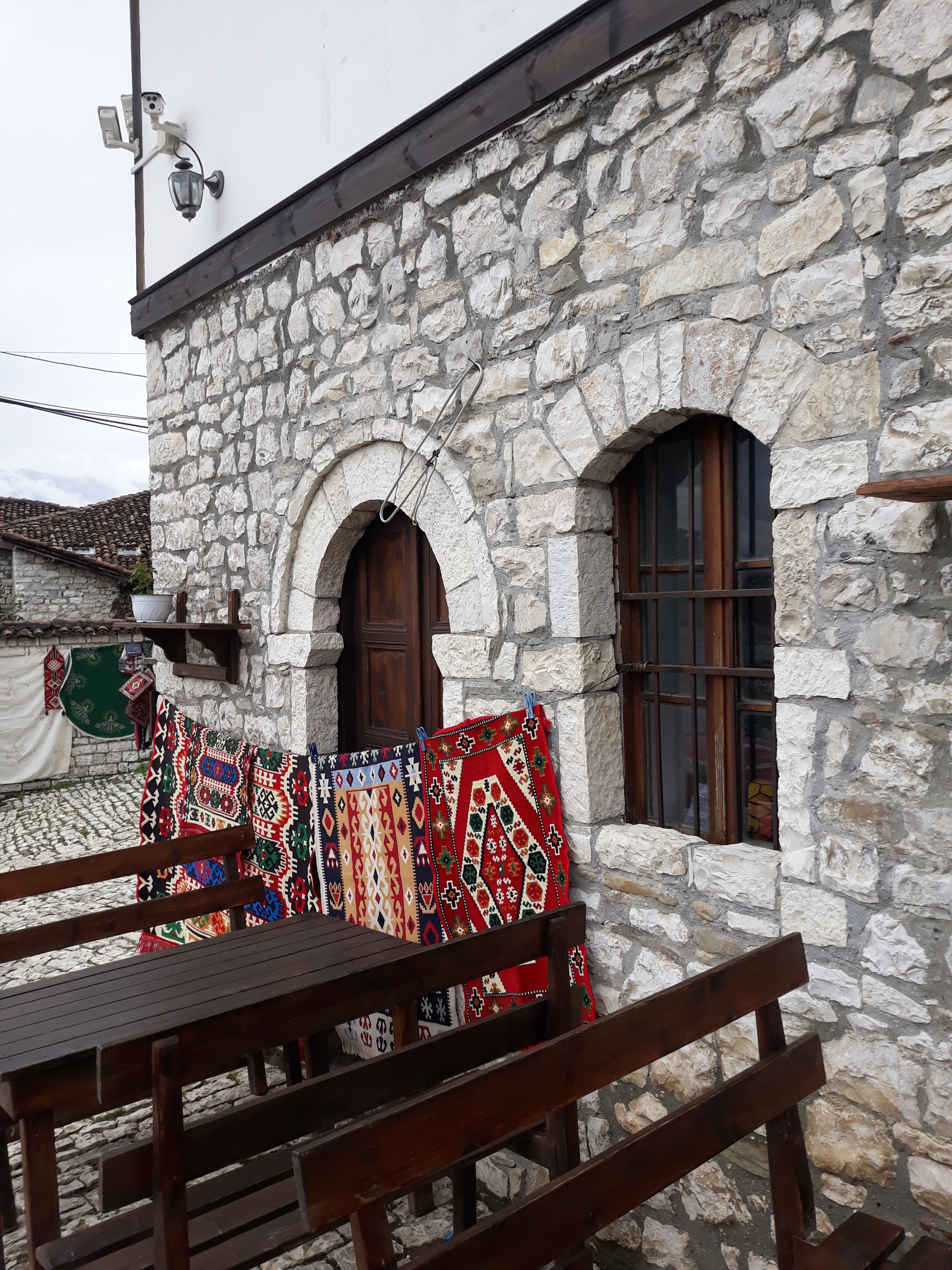 Stone building with traditional woven rugs hanging on a balcony.