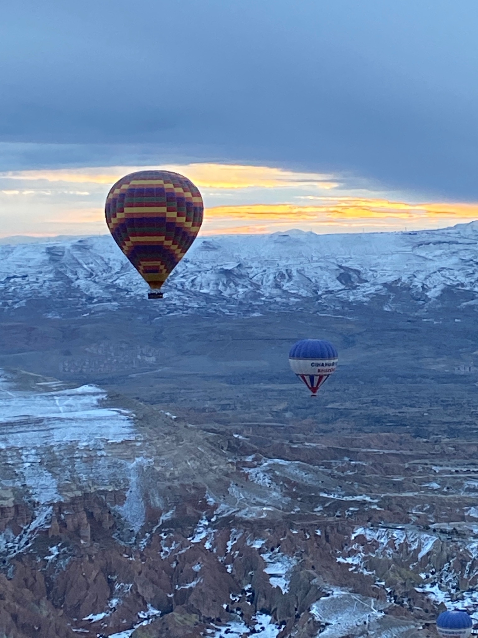 Hot air balloons over snowy Cappadocia landscape.