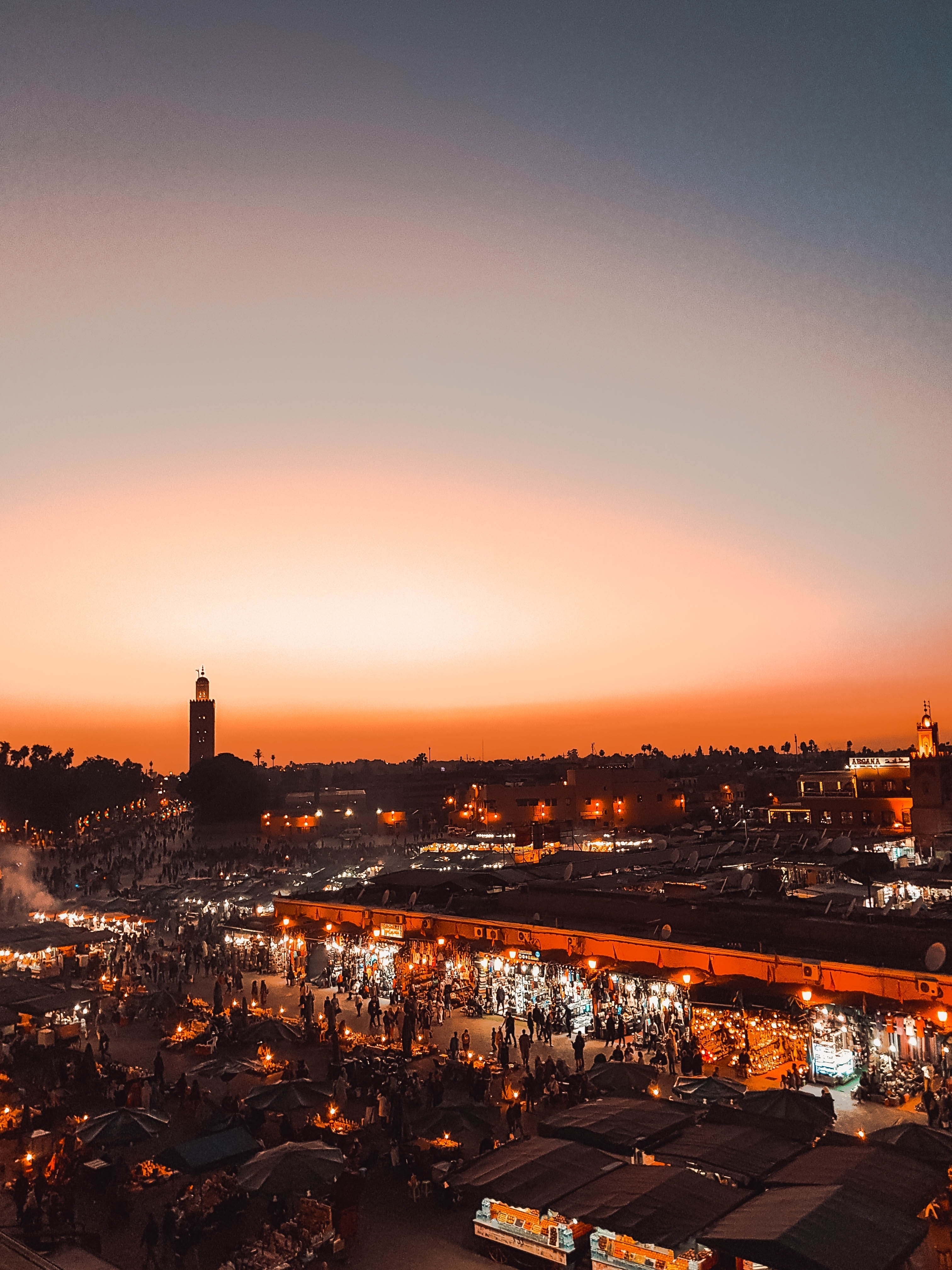 City skyline at sunset with minaret and buildings silhouetted against orange sky.