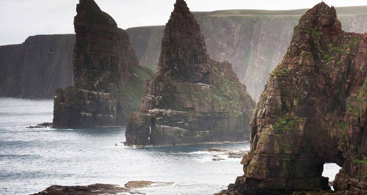 Des formations rocheuses spectaculaires s'élèvent verticalement depuis les vagues déferlantes le long d'une côte écossaise accidentée.