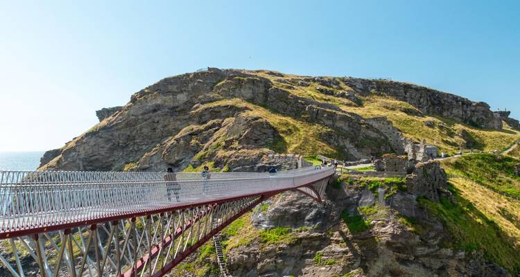 Un passerelle moderne enjambe un promontoire rocheux cornouaillais au château de Tintagel lors d'une journée ensoleillée.