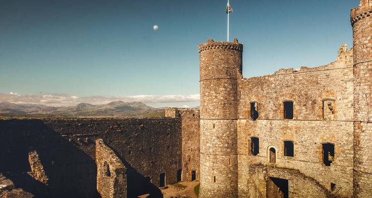 Les murs de pierre baignés de soleil et les tours de l'intérieur d'un château médiéval gallois avec des montagnes au loin.