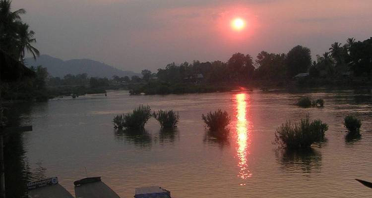 Zonsondergangzicht over een rivier met reflecties en bomen in de verte.
