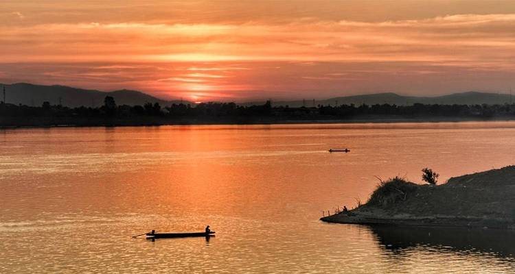 Oranje zonsondergang boven een kalme rivier met twee boten in silhouet.
