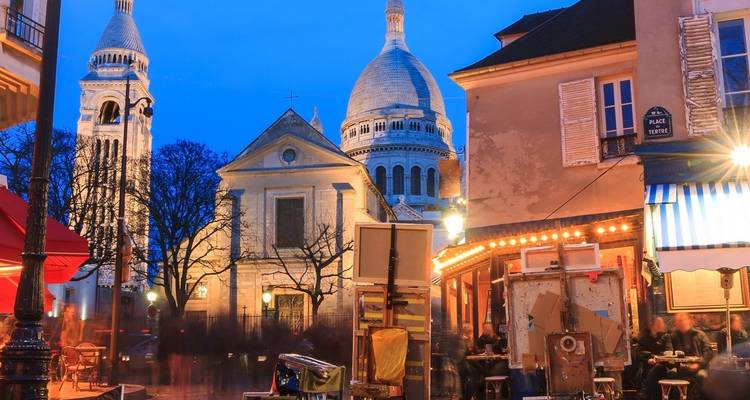 View of the Sacré-Cœur and surrounding buildings lit up at night in Paris.