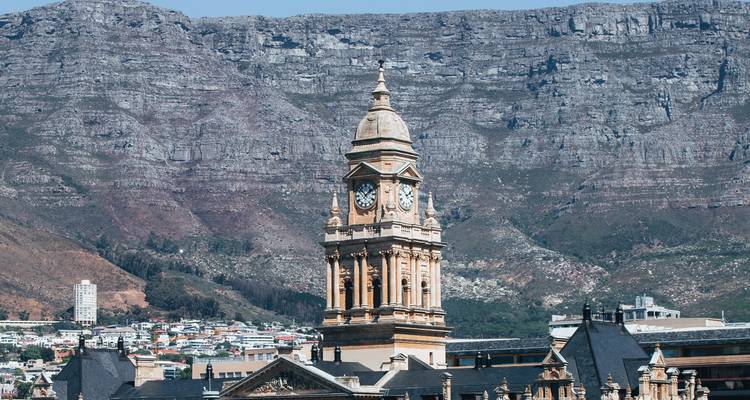 Historic clock tower with mountain backdrop and urban surroundings.