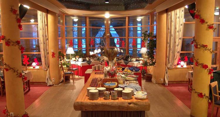 Zone de buffet de restaurant chaleureusement décorée avec des piliers en bois, des ornements rouges festifs et de grandes fenêtres donnant sur la neige à l'extérieur.