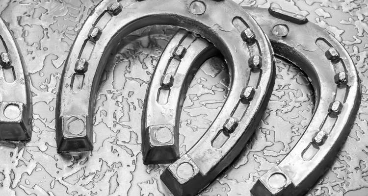 Zwart-wit close-up van enkele metalen hoefijzers die op een geruwde ondergrond liggen.