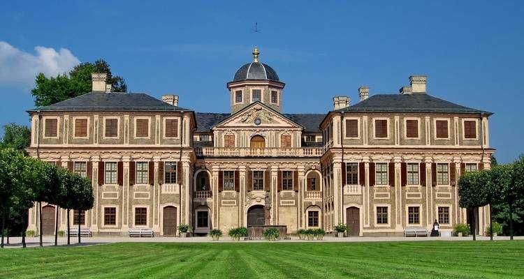 A grand historic building with a manicured lawn and clear blue sky.