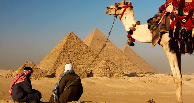 Deux personnes et un chameau au premier plan avec des pyramides en arrière-plan.