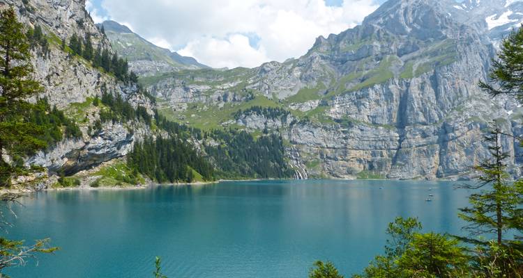 Lac turquoise cristallin entouré de parois rocheuses abruptes et de forêts de conifères.