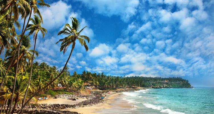 Palmen, die einen wunderschönen Strand unter einem blauen Himmel mit fluffigen Wolken säumen.