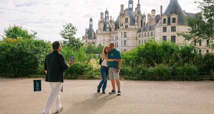 Reiseführer macht ein Foto von einem lächelnden Paar mit den kunstvollen Türmen des Château de Chambord im Hintergrund.
