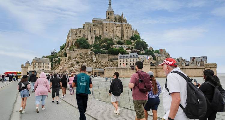 Besucher gehen über den Damm auf die dramatische Abtei von Mont Saint-Michel unter einem leicht bewölkten Himmel zu.