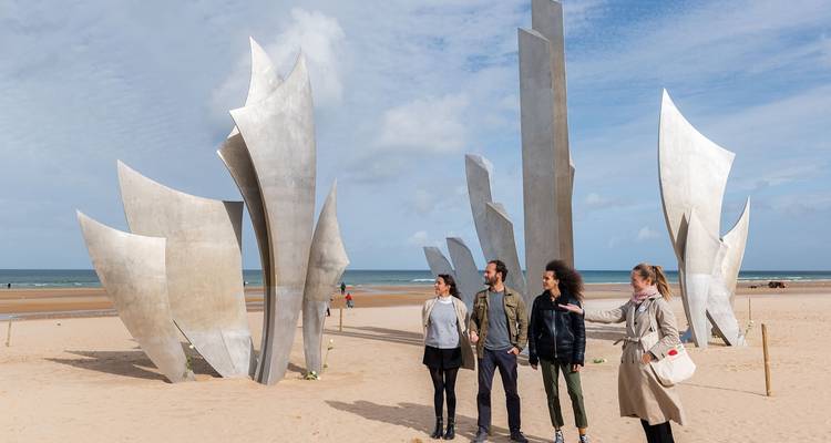 Des gens se promènent sur la plage avec des sculptures à Omaha Beach.