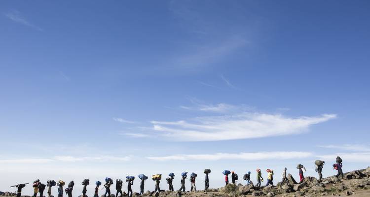 Eine Reihe von Wanderern mit Rucksäcken, die unter einem klaren blauen Himmel wandern.