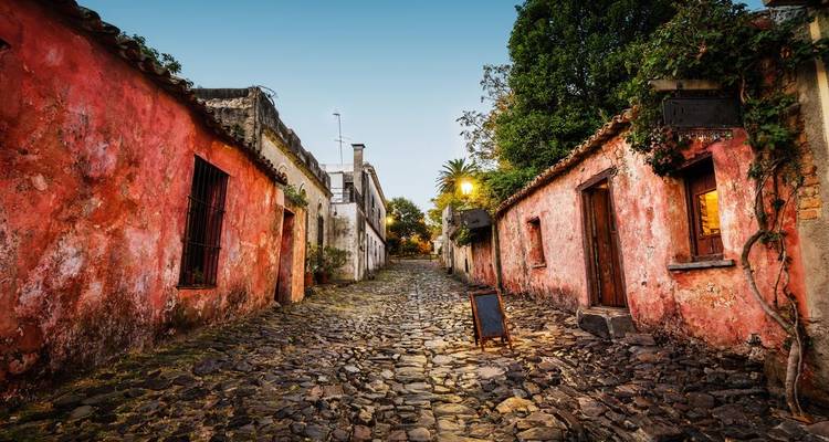 Callejón tranquilo de adoquines flanqueado por casas coloniales rojas y desgastadas al atardecer.