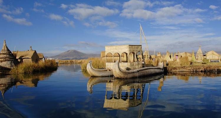 Bateaux et huttes traditionnels en roseau flottant sur les eaux calmes d'un lac avec des montagnes en arrière-plan