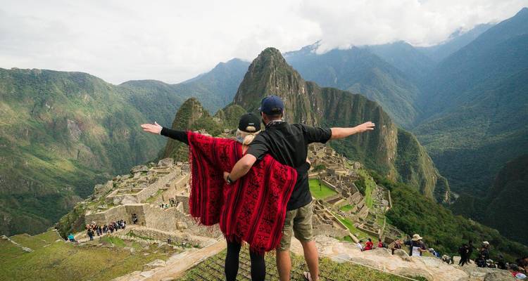 Couple surplombant les ruines du Machu Picchu et les sommets verdoyants des Andes avec les bras étendus