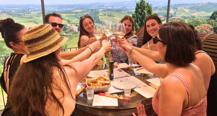 Groep vrienden die met wijnglazen proosten rond een tafel met uitzicht op een wijngaard.