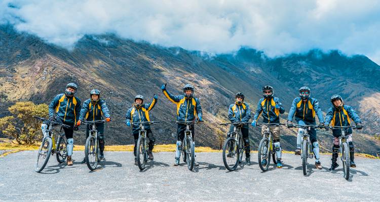 Equipo de ciclismo alineado con bicicletas de montaña contra picos andinos dramáticos y niebla.