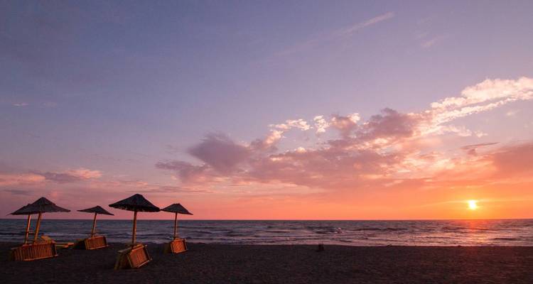 Schilderachtige zonsondergang boven de oceaan met parasols op het strand.