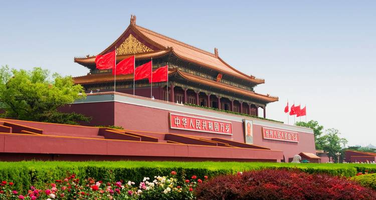 Tiananmen Gate adorned with red flags and Mao portrait stands over manicured gardens.