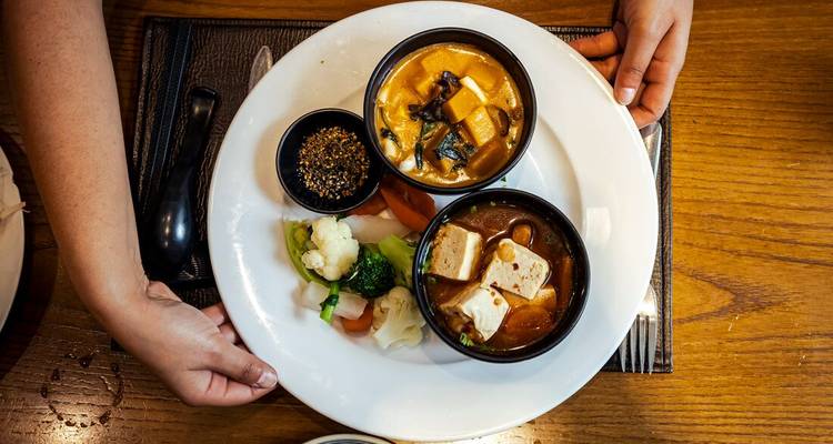 Overhead view of a plated Vietnamese meal with tofu curries, vegetables and dipping spices being served.