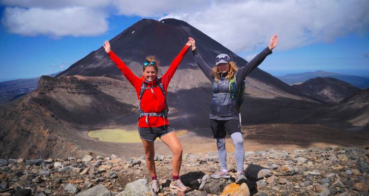 Two hikers celebrating on a volcanic mountain with a crater lake.