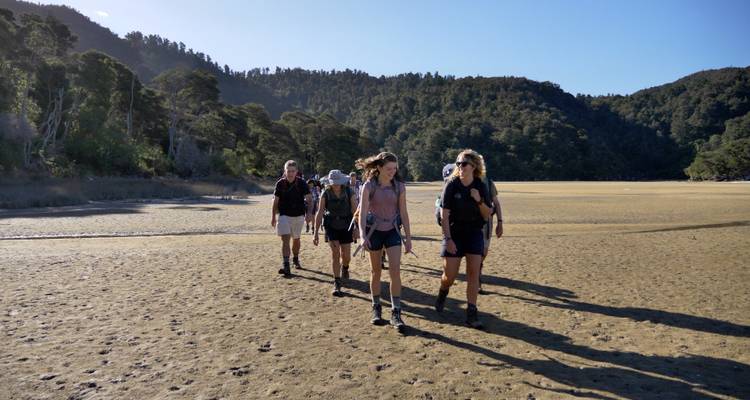 Group of people hiking on a dry, flat landscape with forested hills.