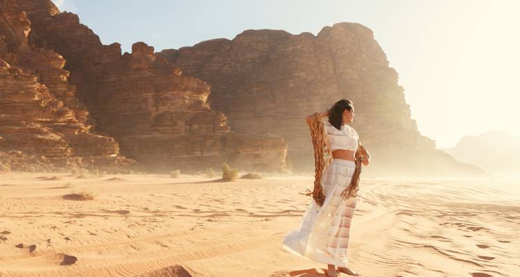 Une femme vêtue d'une robe blanche fluide marche sur les sables dorés du désert de Wadi Rum à l'aube