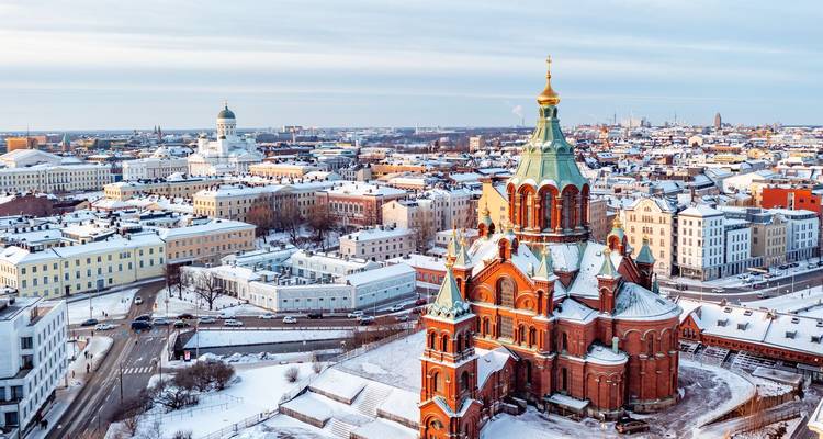 Snow-dusted panoramic skyline of Helsinki featuring the red-brick Uspenski Cathedral and white Helsinki Cathedral under a pale winter sky.